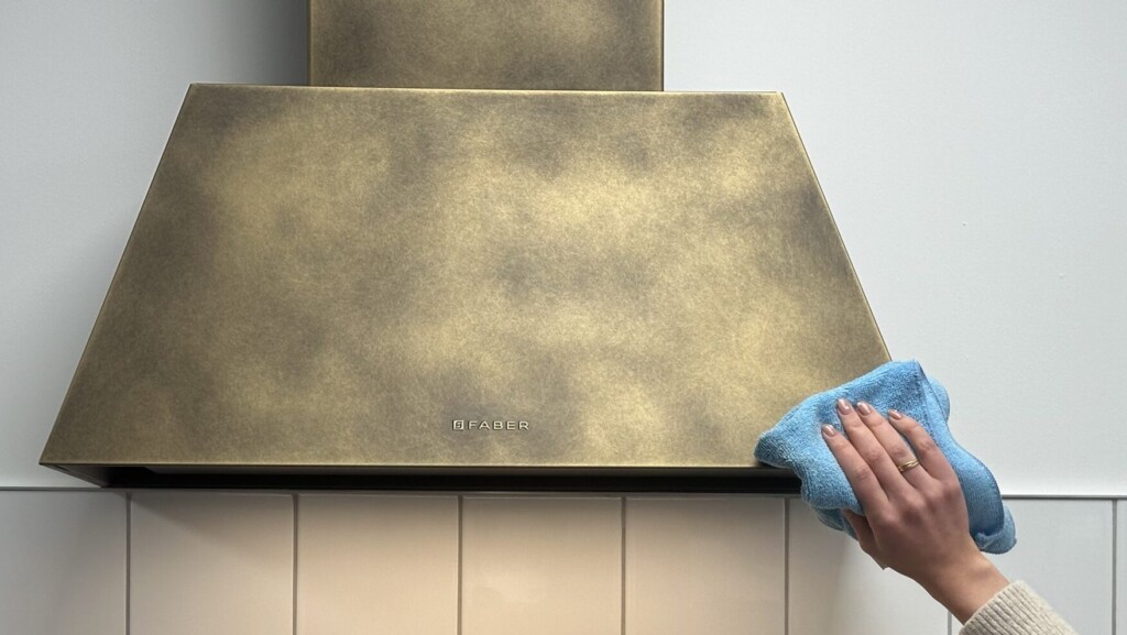 Someone cleaning a brass Faber wall mounted cooker hood with microfibre cloth