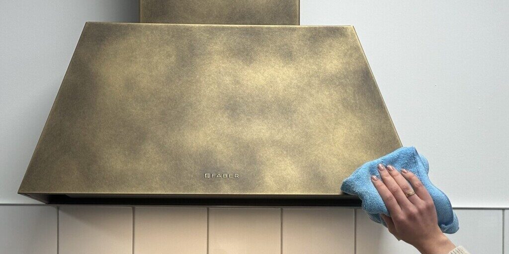 Cooker hood cleaning Someone cleaning a brass Faber wall mounted cooker hood with microfibre cloth